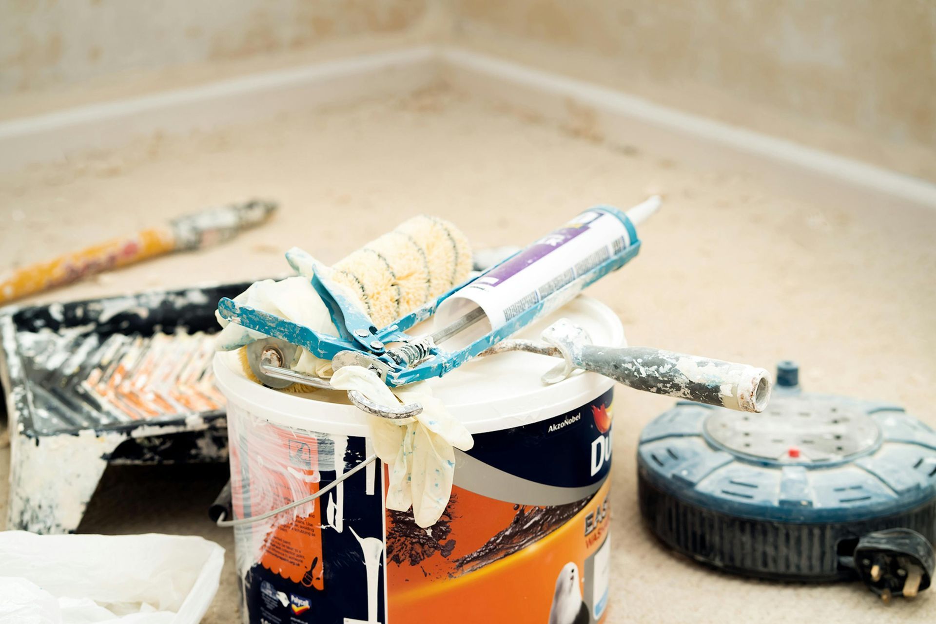 Paint supplies, including rollers, paint tray, and caulk gun, sit on a floor during a home renovation project.