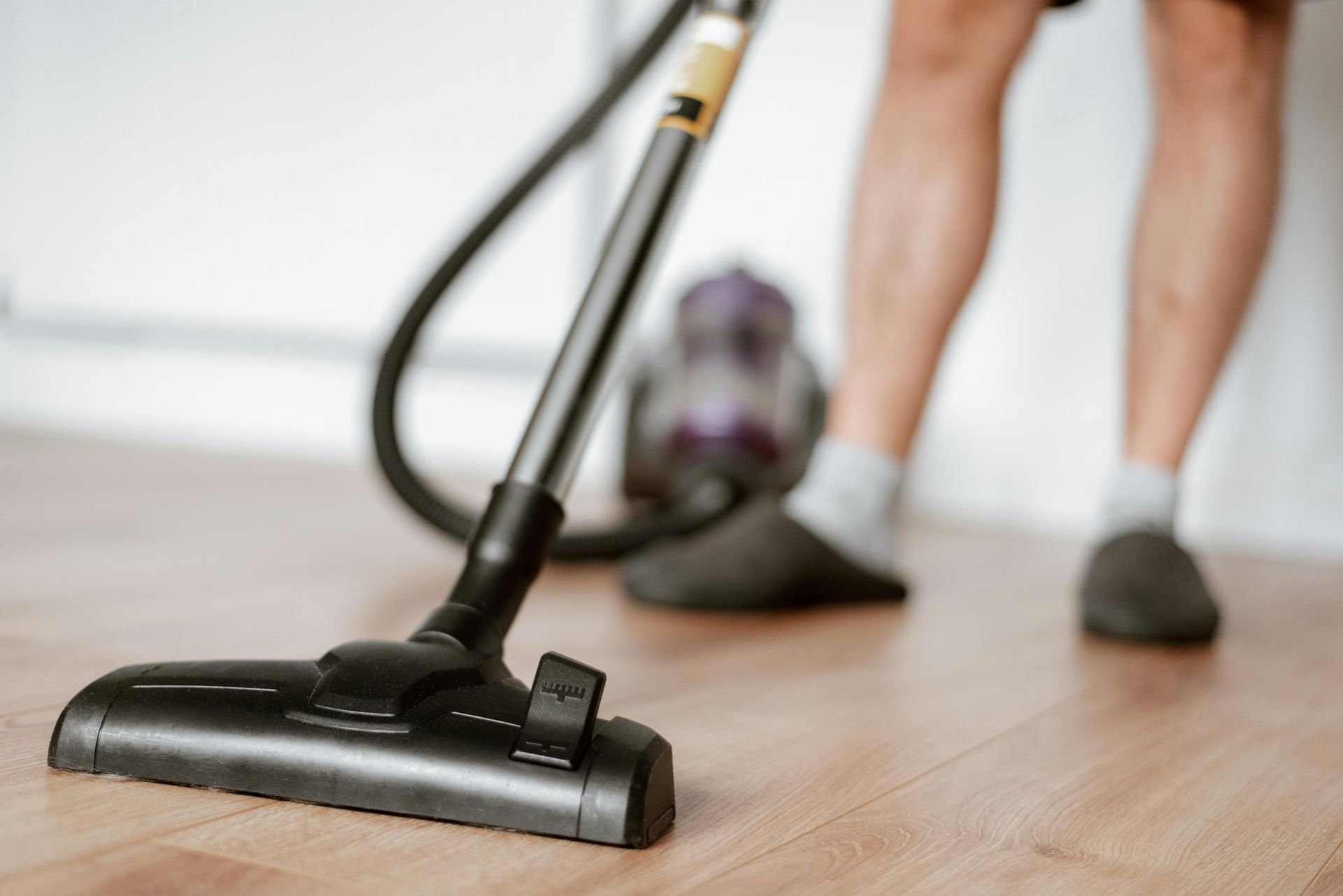 Person vacuuming a wooden floor with a black vacuum cleaner in a room.