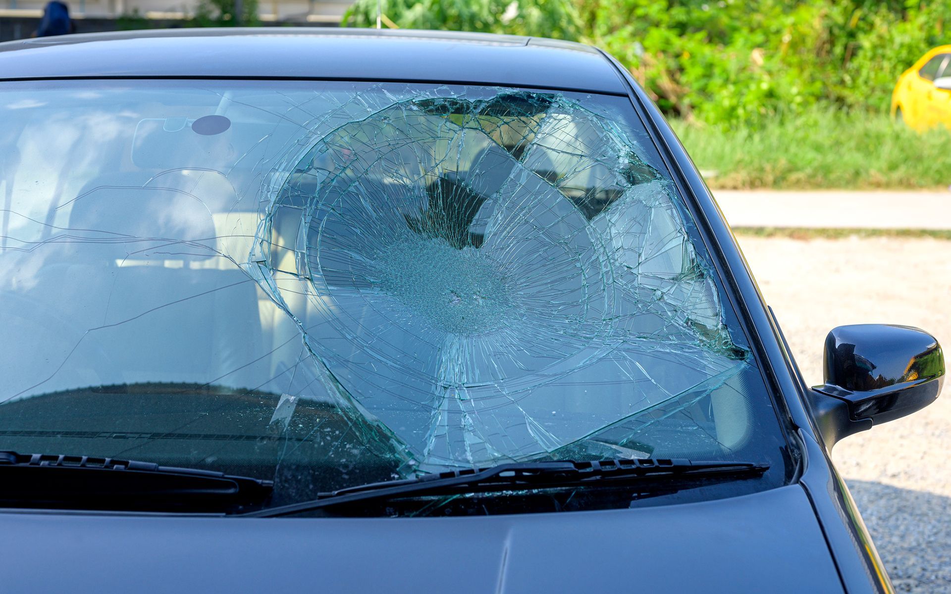 A car with a broken windshield is parked on the side of the road.