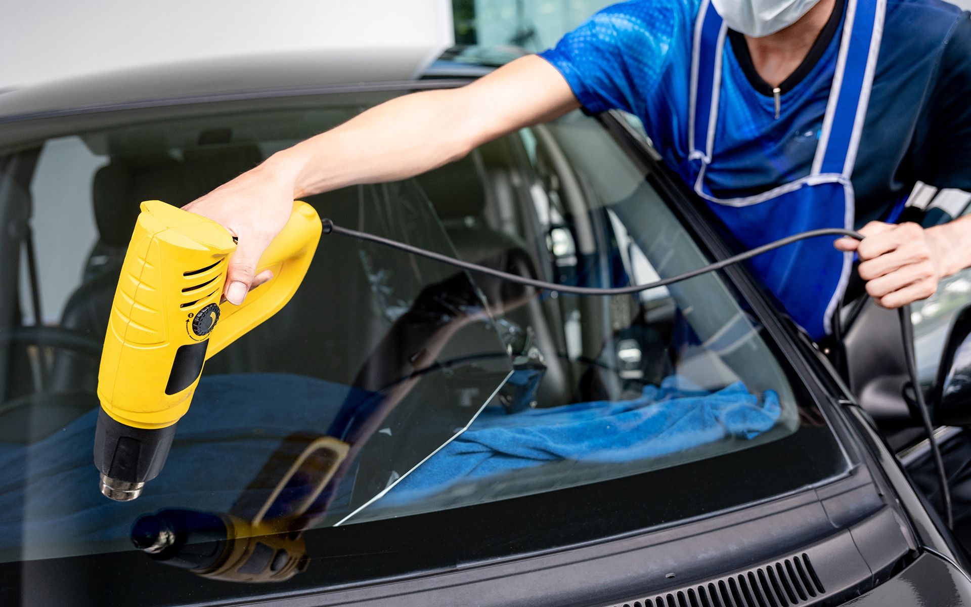 A man wearing a mask is cleaning the windshield of a car.