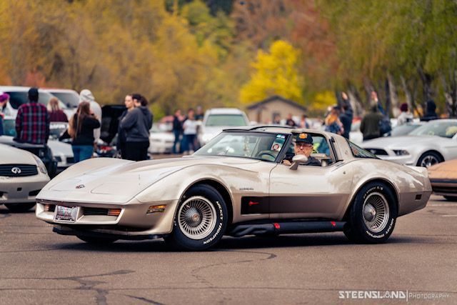 A silver corvette is parked in a parking lot at a car show.
