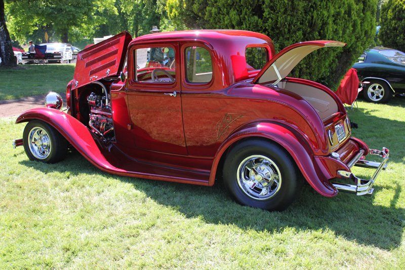 A red car with the hood up is parked in the grass.