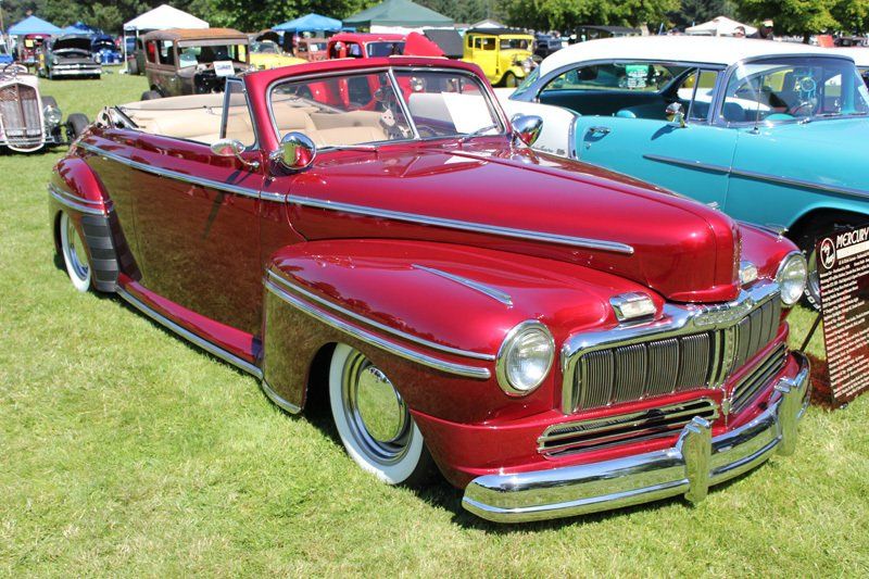 A red convertible is parked in the grass at a car show