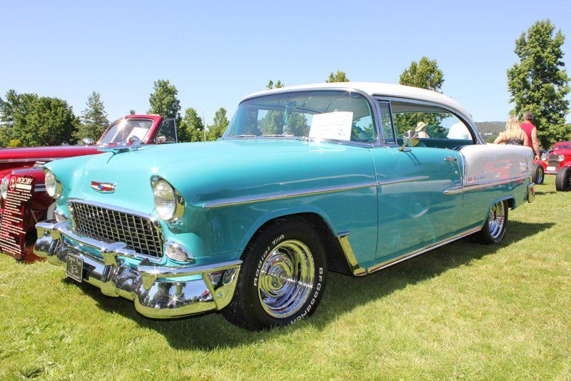 A blue and white car is parked in the grass at a car show.