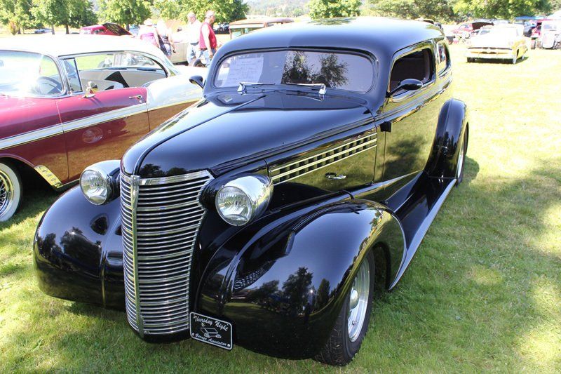 A black car is parked in the grass at a car show