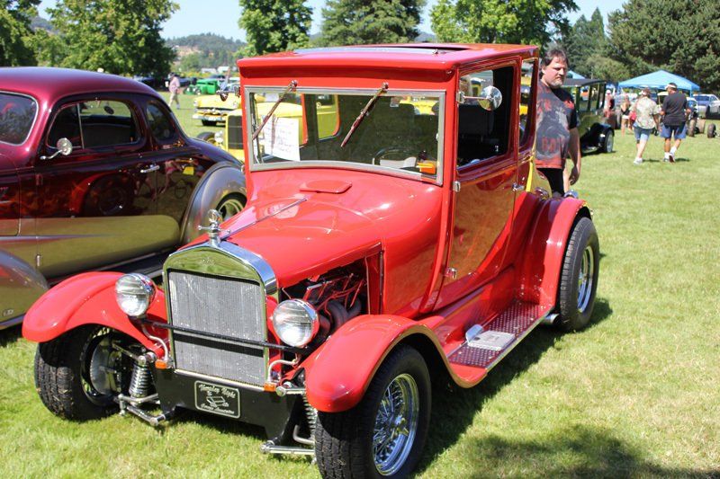 A red car is parked in the grass at a car show.