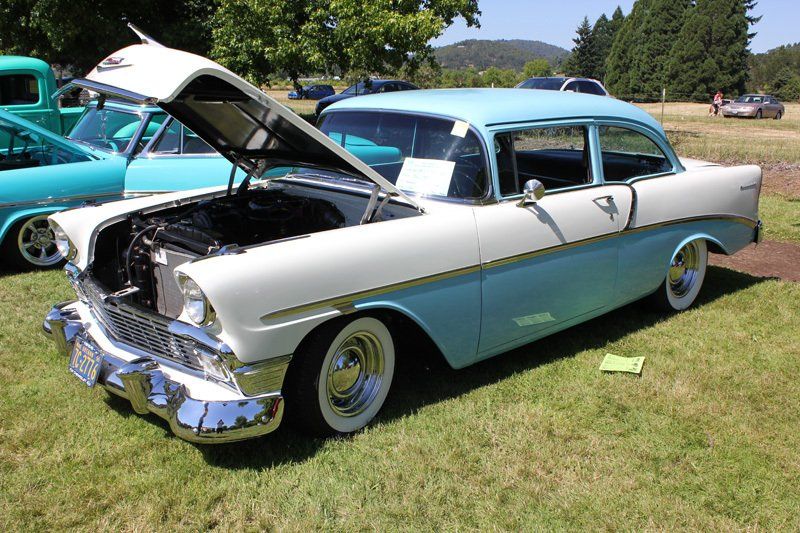 A blue and white car with the hood up is parked in a grassy field