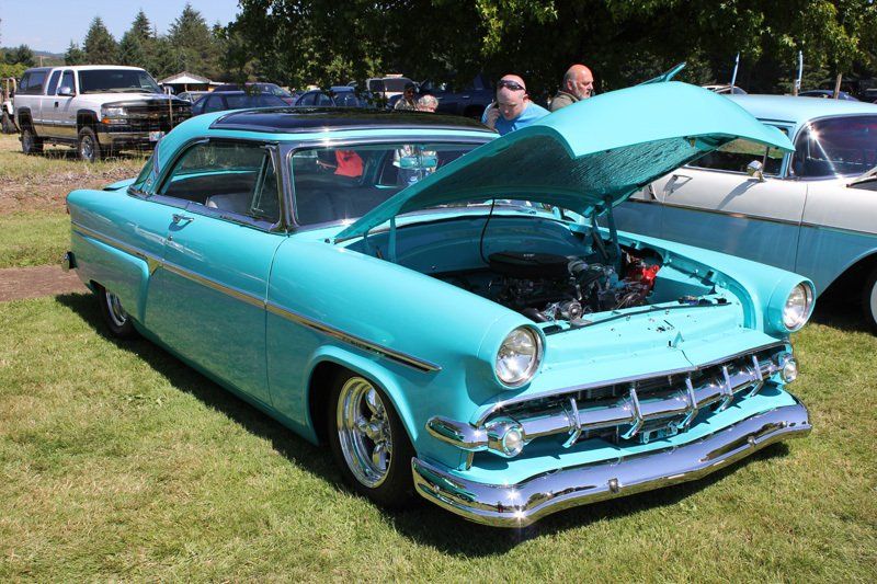 A blue car with the hood open is parked in the grass.