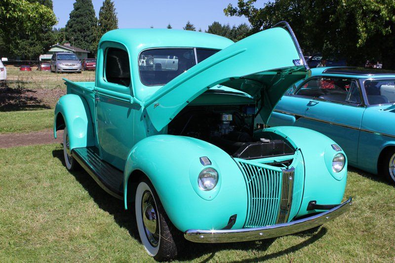 A green truck with the hood up is parked in the grass