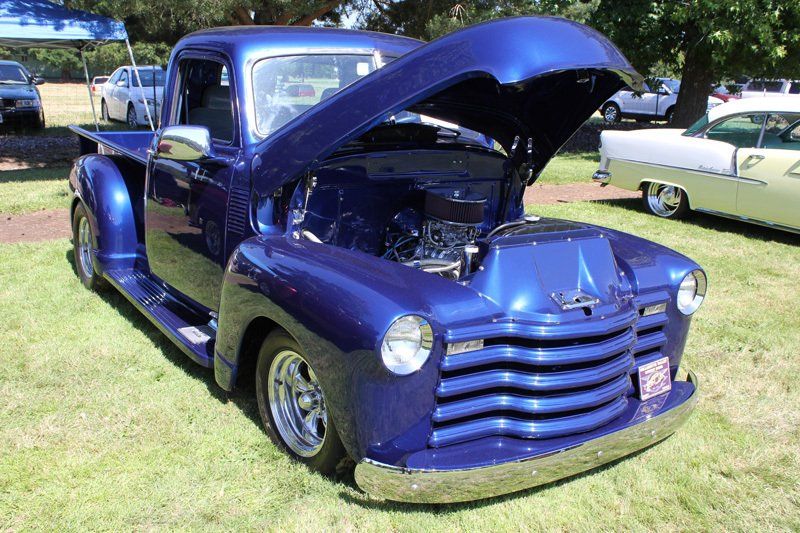 A blue truck with the hood up is parked on the grass.