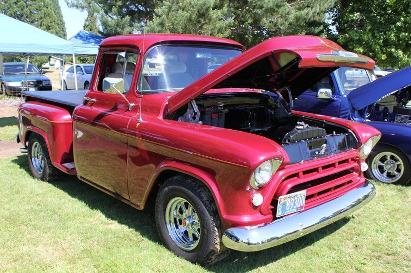 A red truck with the hood up is parked in the grass.