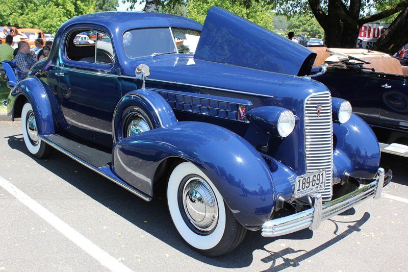 A blue car with white tires is parked in a parking lot