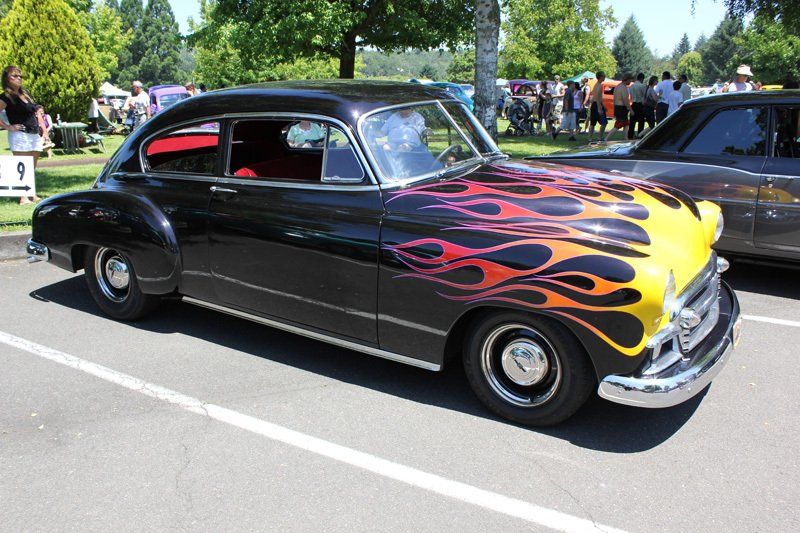 A black car with flames painted on it is parked in a parking lot