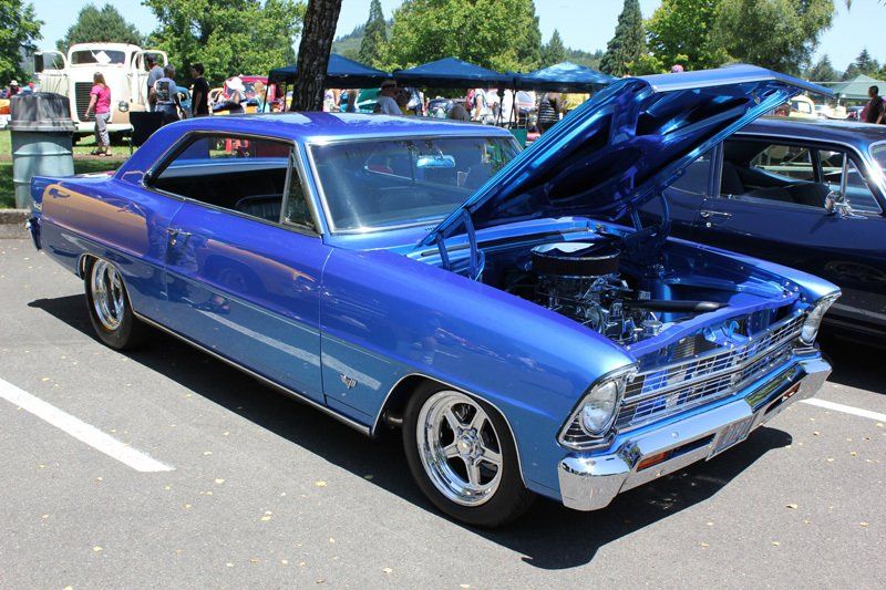 A blue car with the hood up is parked in a parking lot