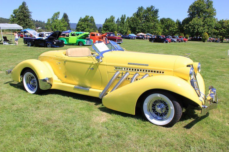 A yellow car is parked in the grass at a car show