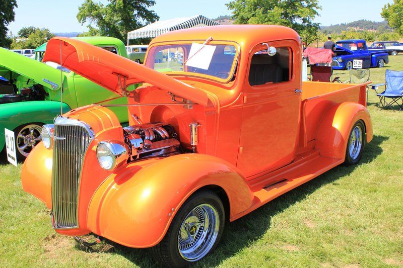 An orange truck with the hood up is parked in a grassy field.