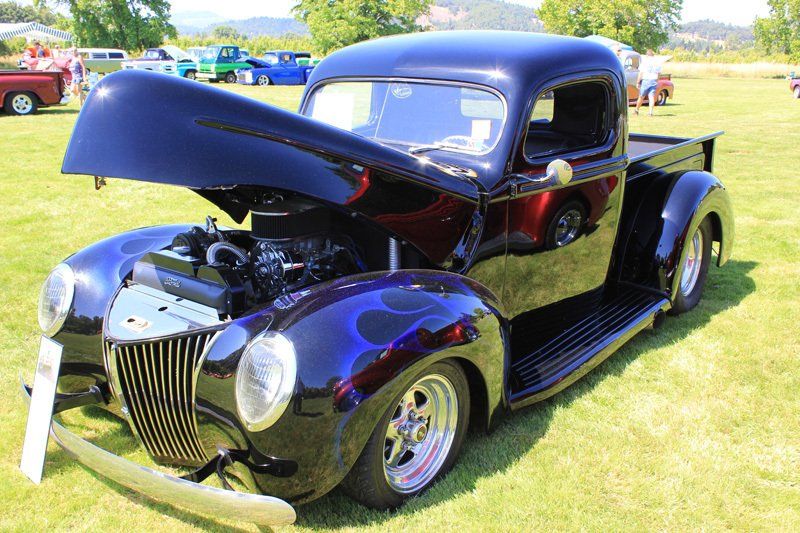 A black truck with the hood up is parked in a grassy field.