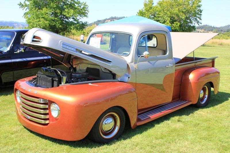 An old truck with the hood up is parked in a grassy field.