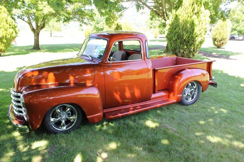 A red truck is parked in the grass in a park.