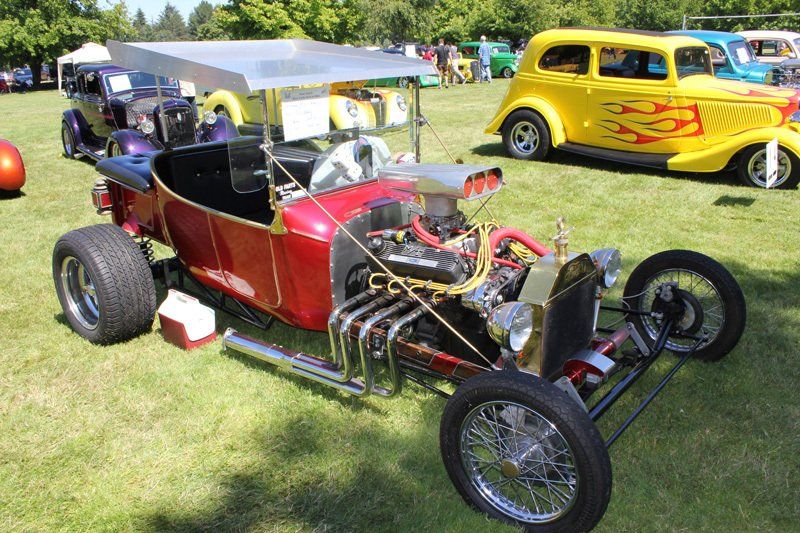A red hot rod is parked next to a yellow car with flames on it