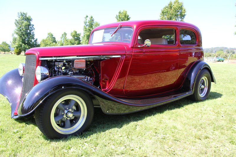 An old red car is parked in a grassy field.
