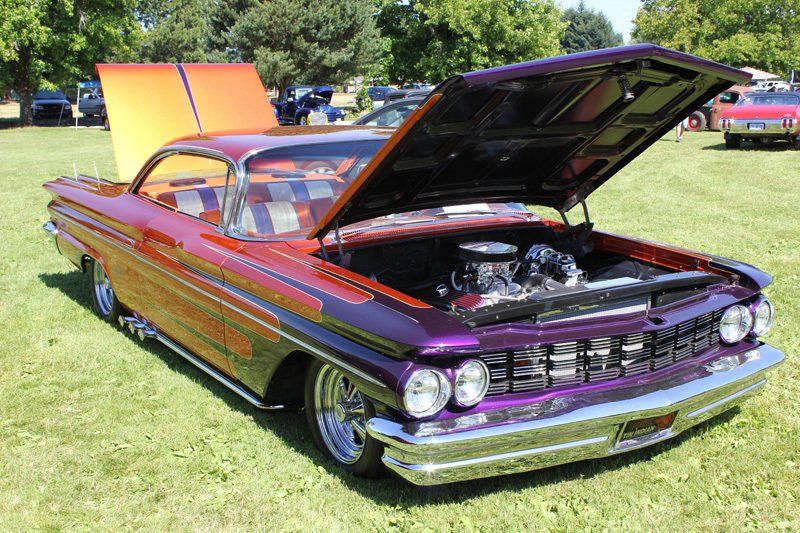 A purple and orange car with the hood up is parked in a grassy field.