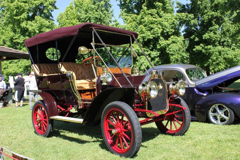 An old car with a canopy is parked in the grass at a car show.