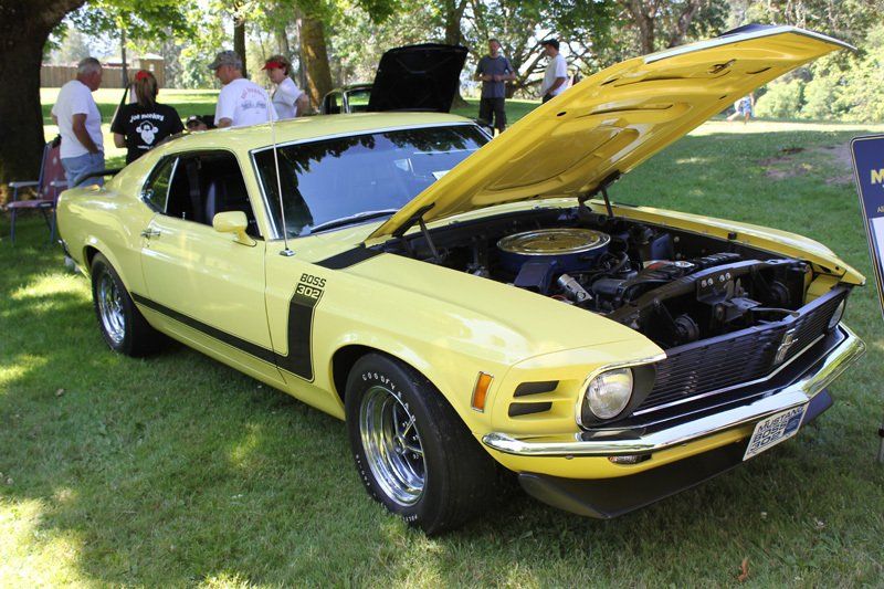 A yellow mustang with the hood up is parked in the grass