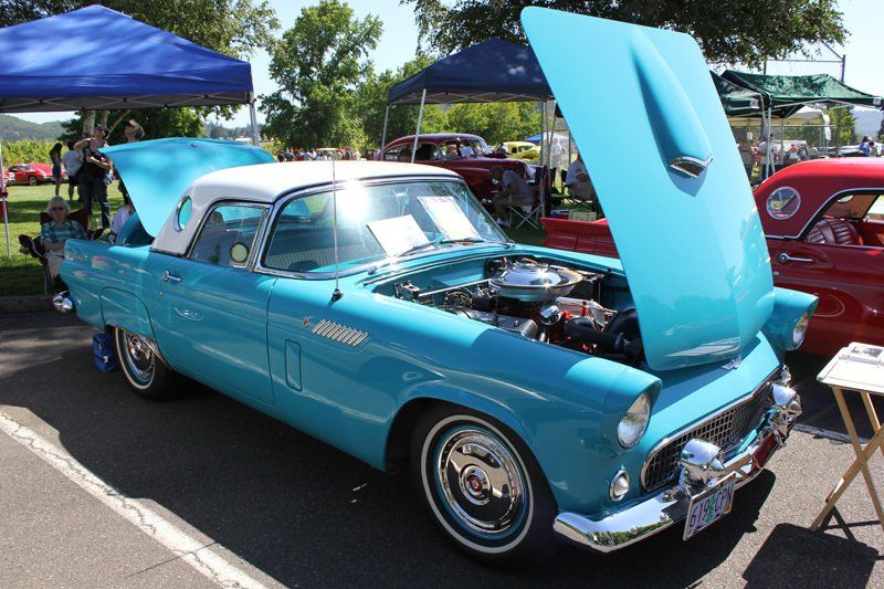 A blue car with the hood up is parked in a parking lot