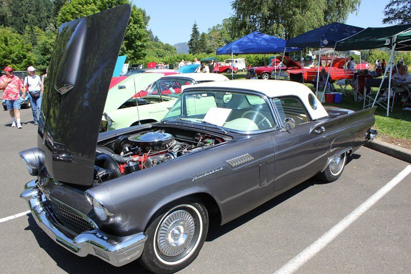 An old car with the hood up is parked in a parking lot