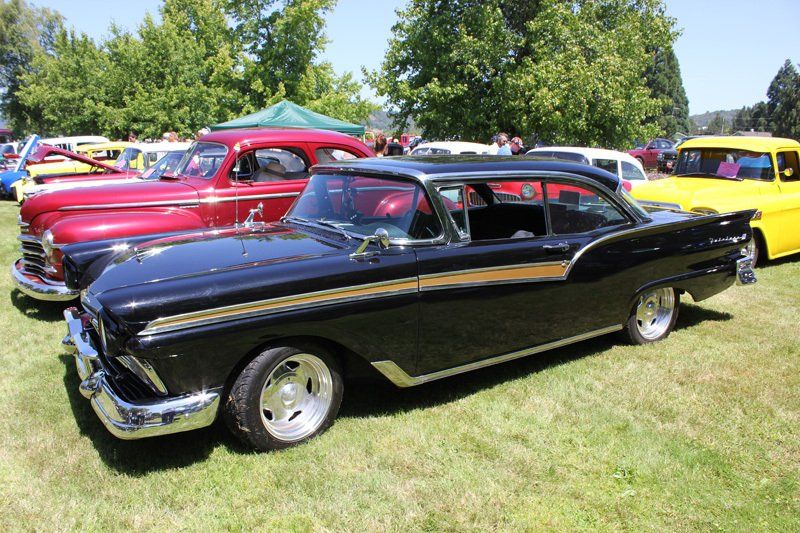 A black car is parked next to a yellow truck at a car show