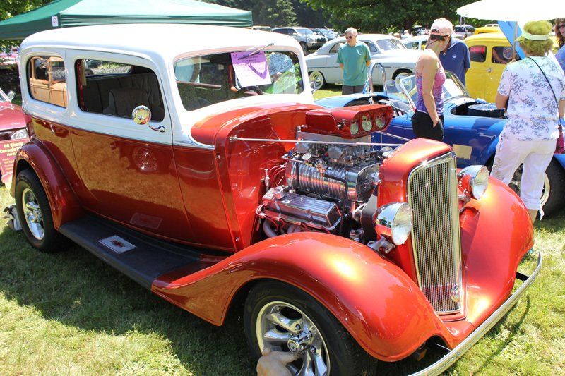A red and white car is parked in the grass at a car show