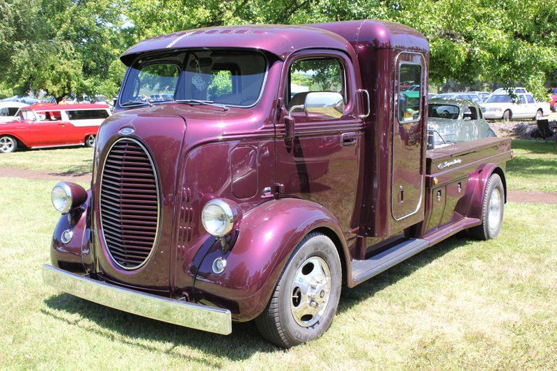 A purple truck is parked in the grass at a car show.