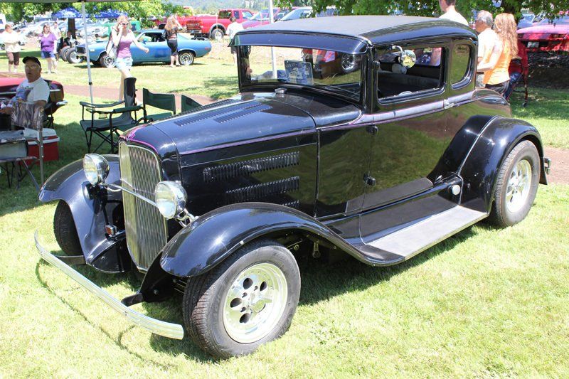 An old black car is parked in the grass at a car show.