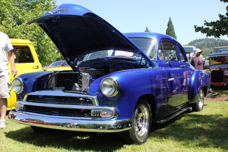 A blue car with the hood up is parked in the grass