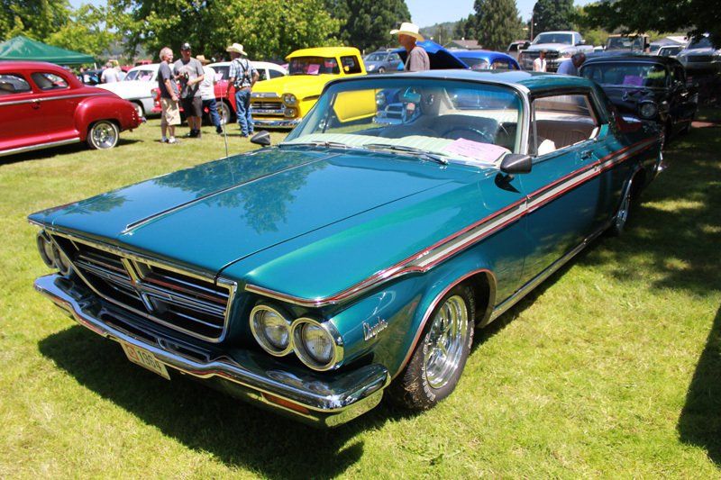 A green car is parked in the grass at a car show
