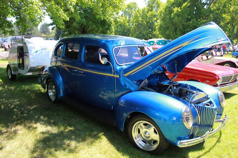 A blue car with the hood up is parked next to a trailer