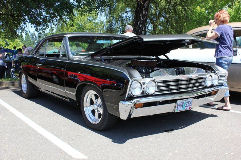A black car with the hood up is parked in a parking lot.