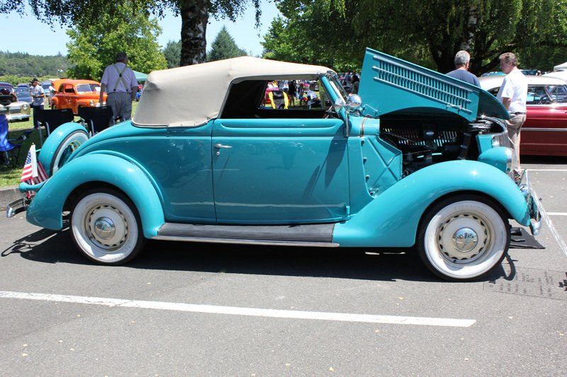 A blue car with the hood open is parked in a parking lot