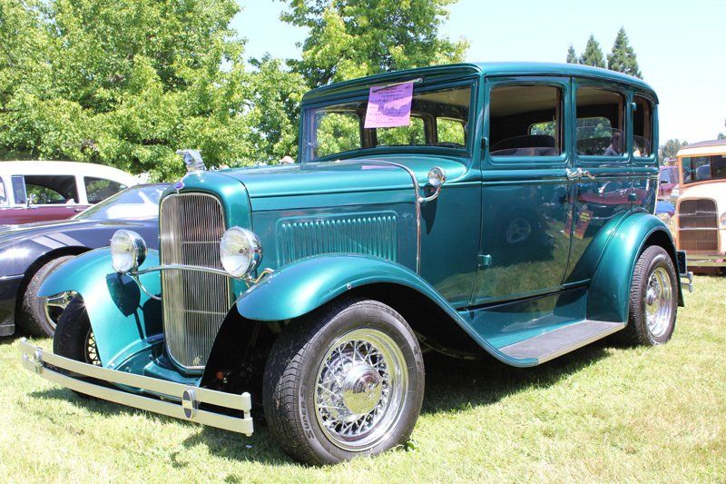 An old green car is parked in the grass at a car show.