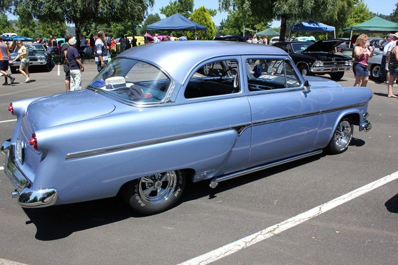 A blue car is parked in a parking lot at a car show