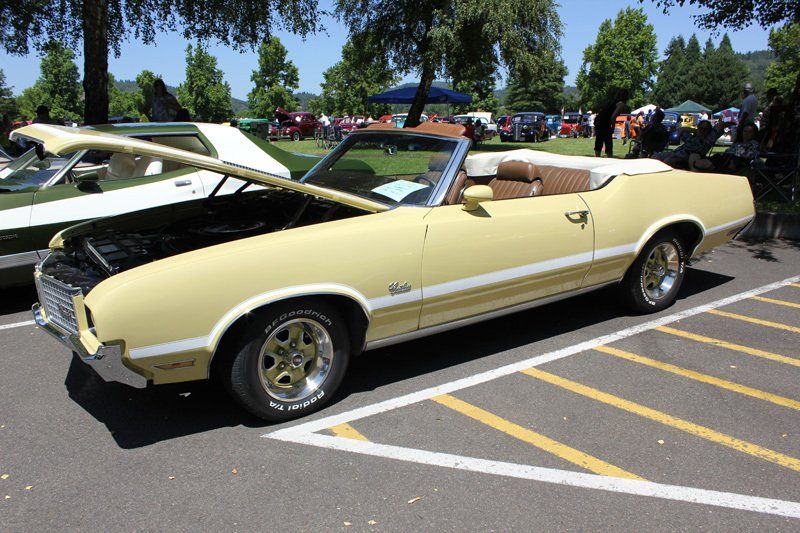 A yellow oldsmobile cutlass convertible is parked in a parking lot