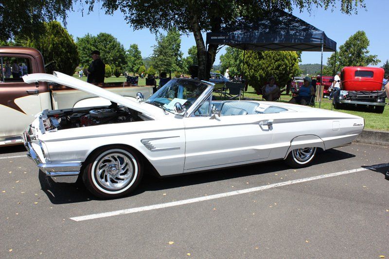 A white convertible with the hood up is parked in a parking lot