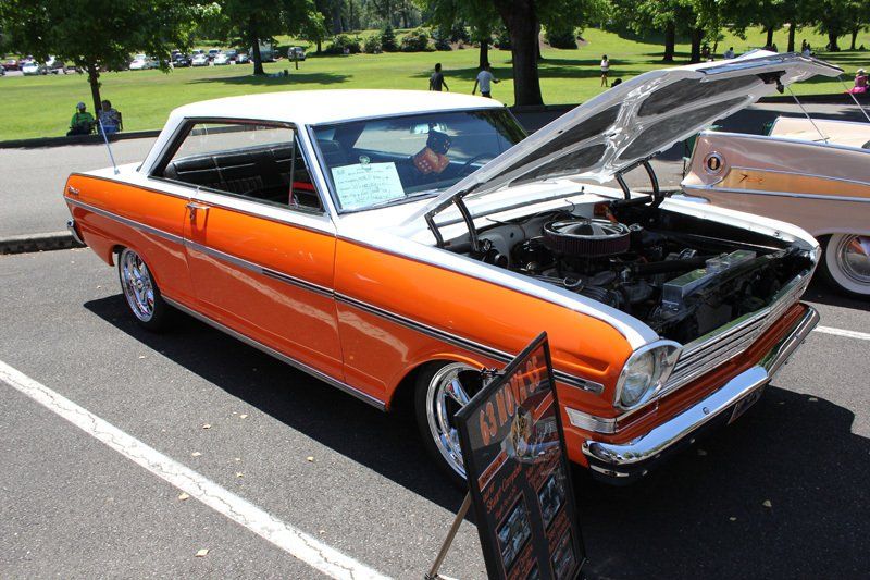 An orange and white car with the hood up is parked in a parking lot