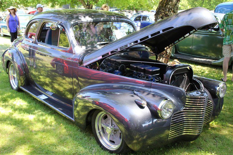 A black car with the hood up is parked in the grass.