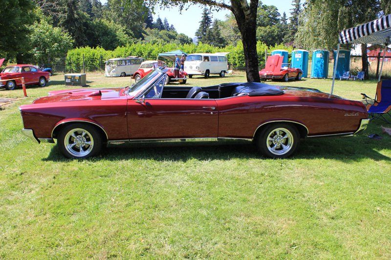 A red convertible is parked in the grass at a car show.