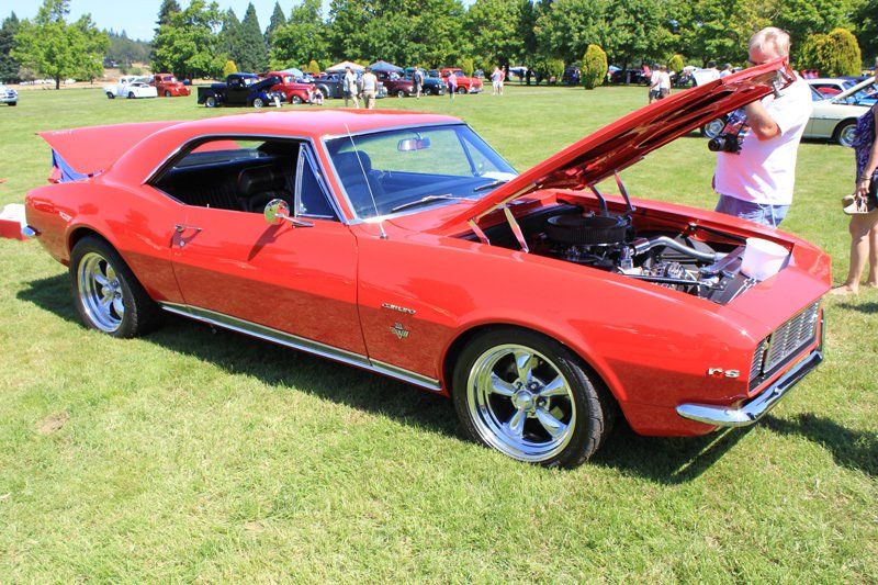 A red car with the hood up is parked in a grassy field.