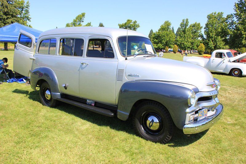 A silver van is parked in the grass at a car show