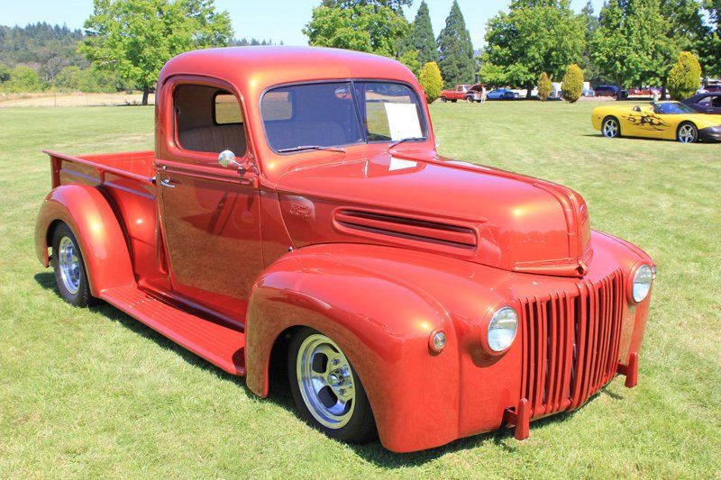 An old red pickup truck is parked in a grassy field.