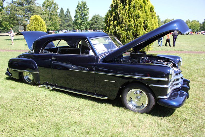 A black car with the hood up is parked in a grassy field